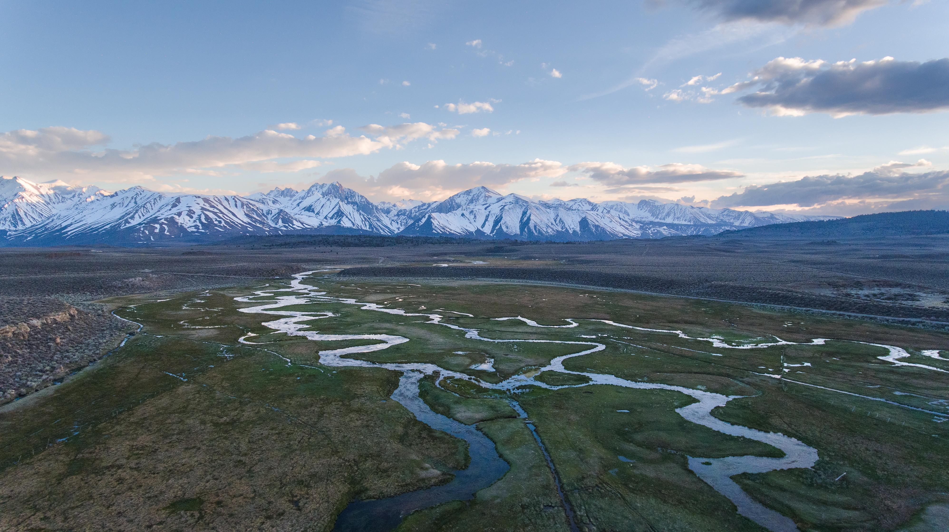 A thumbnail of a flat grassy area with streams and a mountain range with snow in the background, which provides more information on the topic Reduced mountain snowpack 